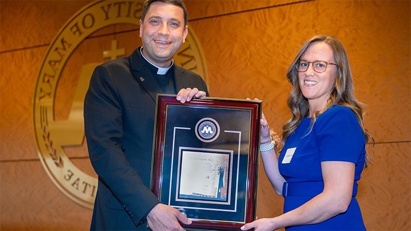 Monsignor with an alumni holding an award plaque